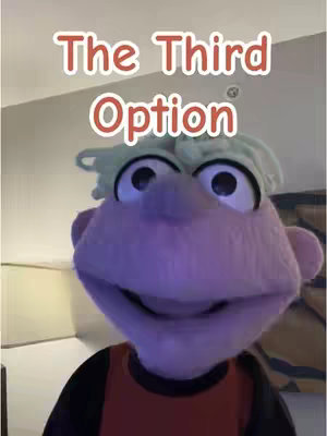 The cover image features a puppet with light green wavy hair and large eyes, set against a blurred background of a room. The puppet's face takes up most of the frame, with text overlayed near the top.