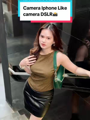 A woman stands in a setting with reflective surfaces, possibly an upscale environment. She wears a sleeveless, brown top, a black leather skirt, and carries a green purse. The image has a posed, stylish aesthetic with a text overlay at the top.