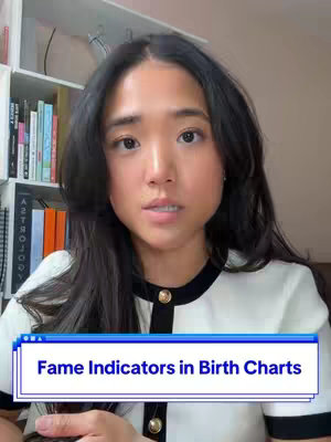 A woman with long dark hair, wearing a white top with black trim and gold buttons, looks directly at the camera. She is centered in the frame, with a background of a bookshelf and wall. A blue and white text box at the bottom of the frame reads "Fame Indicators in Birth Charts".