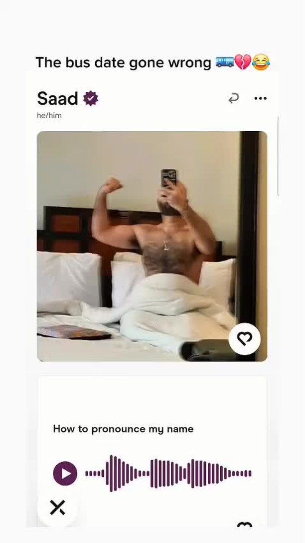 The image shows a man in a hotel room flexing his arm, appearing to be in bed, with a dating app user interface at the top.