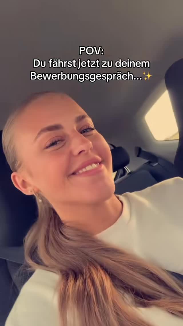 A selfie taken from inside a car. The creator, a blonde woman with her hair in a ponytail, smiles at the camera while seated. Text overlayed at the top says "POV: Du fährst jetzt zu deinem Bewerbungsgespräch... ✨". The background is out of focus, but suggests a car interior.