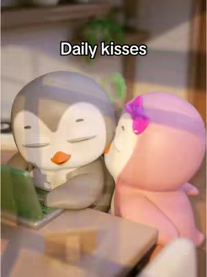 The image shows two cartoon penguin figures.  One, colored in gray, has its eyes closed and is wearing a small green accessory.  The other is pink and has a pink bow. They are in close proximity to each other, and a text overlay reading 'Daily kisses' is present. The scene appears to be indoors.