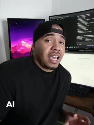 A man with a black cap and black shirt is centered, with a computer and multiple computer screens in the background.