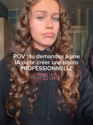 The image shows a young woman with curly brown hair and a black hoodie. The text overlay reads: POV: tu demandes à une IA de te créer une photo PROFESSIONNELLE. The woman has a slightly pensive expression, with her lips pursed. The background is a blurred room interior.