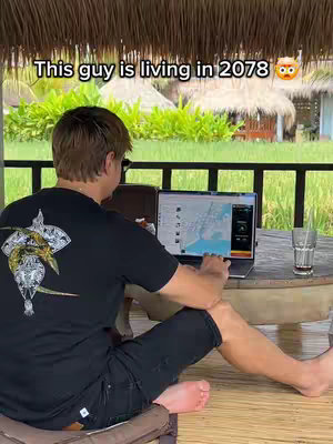 The cover image shows a man sitting at a table outdoors, using a laptop. The man is seen from the back, wearing a black t-shirt with a graphic on it, and black shorts. A laptop is open in front of him, displaying some kind of map or data visualization. Next to the laptop is a glass of liquid. The background shows foliage, suggesting a tropical location. The sun is shining, and everything look pretty. In the upper part of the shot, there is a hook, which says 'This guy is living in 2078' with a surprised face emoji.