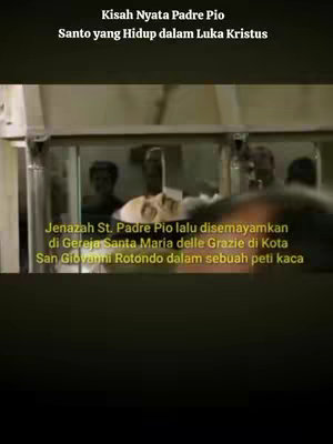 The image is a vertical video frame. The top portion of the image has text overlays. The background is a blurred indoor setting, possibly a church or a similar religious structure. The central focus is on a glass case, with what appears to be a person's face visible within, likely Padre Pio. The image is in muted colors with a somber tone.