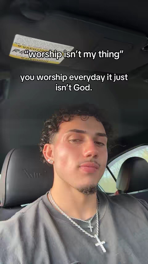 The cover image features a young man with curly hair, wearing a gray t-shirt and a silver chain with a cross pendant. He's in a car, looking at the camera with a neutral expression. Text overlays, in a simple white font, state: "worship isn't my thing" and "you worship everyday it just isn't God." The background shows the car's interior.