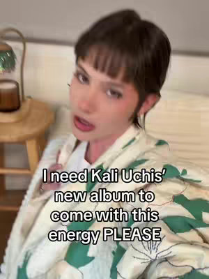 A woman with short dark hair and a white undershirt is speaking to the camera. SHe wears a floral jacket with green accents. Text overlaid on the image reads "I need Kali Uchis' new album to come with this energy PLEASE".