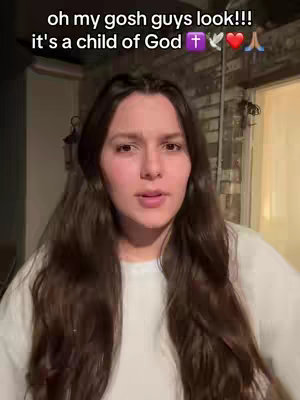 A woman with long brown hair is centered in the frame, looking directly at the camera. Text is overlaid at the top, and the overall setting appears to be indoors. The woman is fair-skinned and wears a white t-shirt.