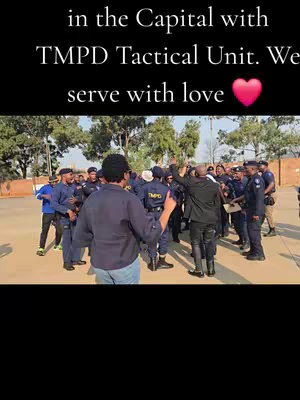 The cover image shows a group of people, primarily police officers in dark blue uniforms, gathered outdoors. A person in a black jacket and another in a blue shirt are facing and addressing the group. The text overlay at the top states "in the Capital with TMPD Tactical Unit. We serve with love", accompanied by a pink heart emoji, setting the scene. The background indicates an outdoor setting during daylight hours.