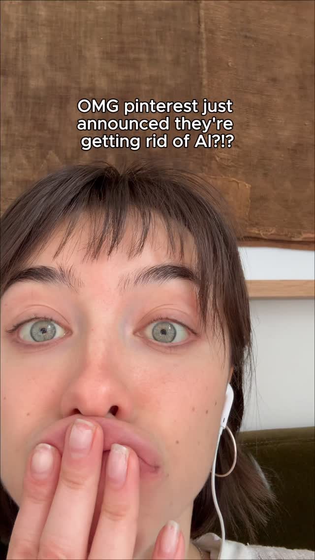 A close-up shot of a young woman with brown hair, blue-green eyes looks directly at the viewer. Her hand is near her mouth covering it slightly, with the lips a little bit open, revealing the bottom teeth. The text overlay reads 'OMG pinterest just announced they're getting rid of AI?!?!'. The background is a light brown, and the overall composition is focused on the woman's surprised expression.
