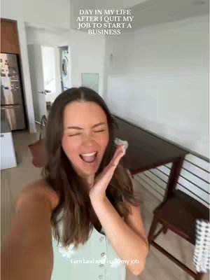 A woman with long brown hair smiles widely, holding her right hand near her face. Text overlays at the top read "DAY IN MY LIFE AFTER I QUIT MY JOB TO START A BUSINESS." The background shows an entryway with a door and visible furnishings. The setting appears to be inside a home, with natural light.