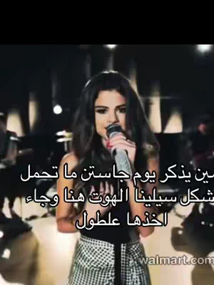The image shows Selena Gomez singing into a microphone on stage. She has dark hair and is wearing a black top and a patterned skirt. The background is dark.