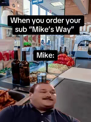 The cover image shows a meme format with text overlayed on an image of a restaurant setting with "Mike" looking up from below a counter of prepared food inside of a Jersey Mike's, with text overlaid on the top of the image, and a black rectangle with white text over his face. The restaurant's setting features stainless steel counters, food displays, bottles, and the background shows a customer. The color palette is a mix of natural and warm restaurant lighting.