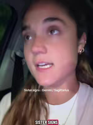 A selfie-style shot of a young woman in a car, looking towards the left. The lighting is dim with green hues, and a white t-shirt is visible.
