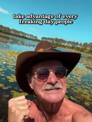 An outdoor selfie of a man wearing a brown cowboy hat and sunglasses, standing in front of a body of water. The text overlay reads: "take advantage of every freaking day people".