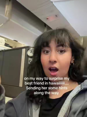 A young woman with dark hair and a surprised expression is the focus, set against a background suggestive of an airplane interior. Text overlays on the image describe the context: "on my way to surprise my best friend in hawaiiiiiii.... Sending her some hints along the way". The composition emphasizes the creator's excitement.