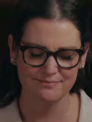A close-up shot of actress Melanie Lynskey with glasses and closed eyes, appearing thoughtful. The composition is a head and shoulders portrait with a neutral background.