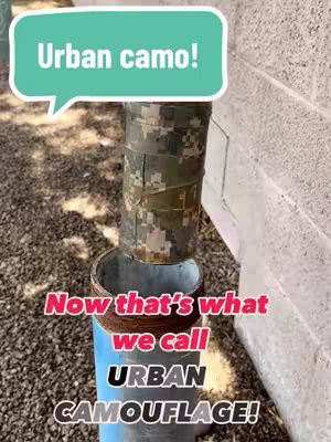 The image features a vertical composition showing a camouflage-taped pipe segment set in an outdoor setting. The pipe, wrapped in a mix of green, brown, and tan camouflage tape, is placed on top of a blue pipe segment with a rust-colored band. The pipes are set against a rough concrete wall to the right, and what appears to be gravel or stone on the ground in the foreground, with a speech bubble containing the words 'Urban camo!' at the upper left. Below this, another text overlays says, 'Now that's what we call URBAN CAMOUFLAGE!'