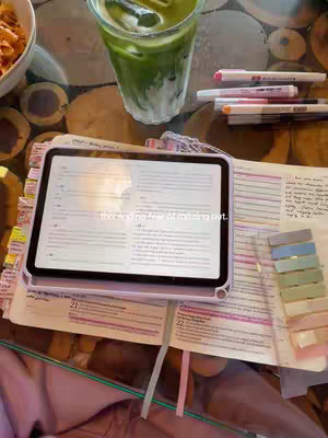 A cover image showcasing a well-lit Bible study setup in a cafe. On a wooden-look table is an open Bible with visible notes, a tablet displaying text, a glass of green drink and some pens.