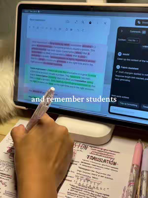 A hand holding a pen is writing on a study sheet while the screen of an open tablet displaying notes shines in the background.  The tablet has text highlighted in yellow and pink, with a comment section open on the right.  Text at the bottom reads "and remember students".  Additional study sheets and pink, clear pens are on the table.