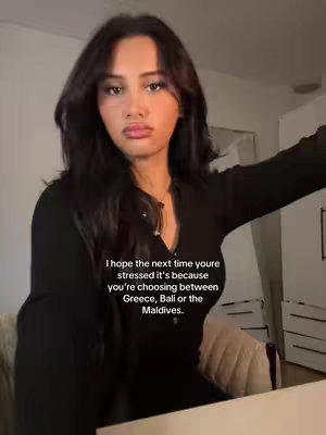 A woman with long dark hair and a black top leans slightly forward, looking at the camera with a neutral expression. Text overlays on the image.