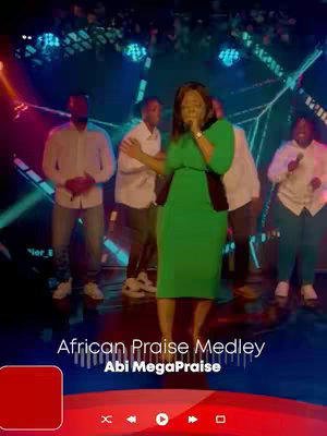 The cover image shows a live performance with a woman singing into a microphone, dressed in a green dress, and surrounded by several other people who appear to be supporting singers. The background is dark and lit up with colorful lights, conveying a concert atmosphere. Text at the bottom displays the song title and the artist's name.