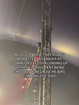 The image shows a high-angle, nighttime shot of a tall metal structure, possibly part of a concert stage. A person is climbing the structure. Overlaid on top is white text, describing an incident at a festival where a person's actions resulted in a shutdown. The image is dark, with some lights and fog.