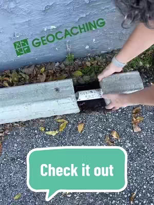 The image shows a geocaching scene. An individual's hands are interacting with sections of concrete and a hidden container, likely a geocache. The background has the word 'geocaching' in green with a logo.