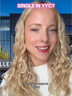 A medium shot of a woman with long wavy blonde hair and a white sweater, smiling at the camera. There is text overlaid on the top of the image. Behind her, there is a building with reflective glass and some greenery.