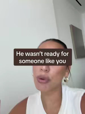 The image shows a woman in a white top speaking to the camera. A brown rectangular overlay displays the text "He wasn't ready for someone like you". The background is a light beige wall with a picture frame on the right. The woman is in focus, with neutral lighting.