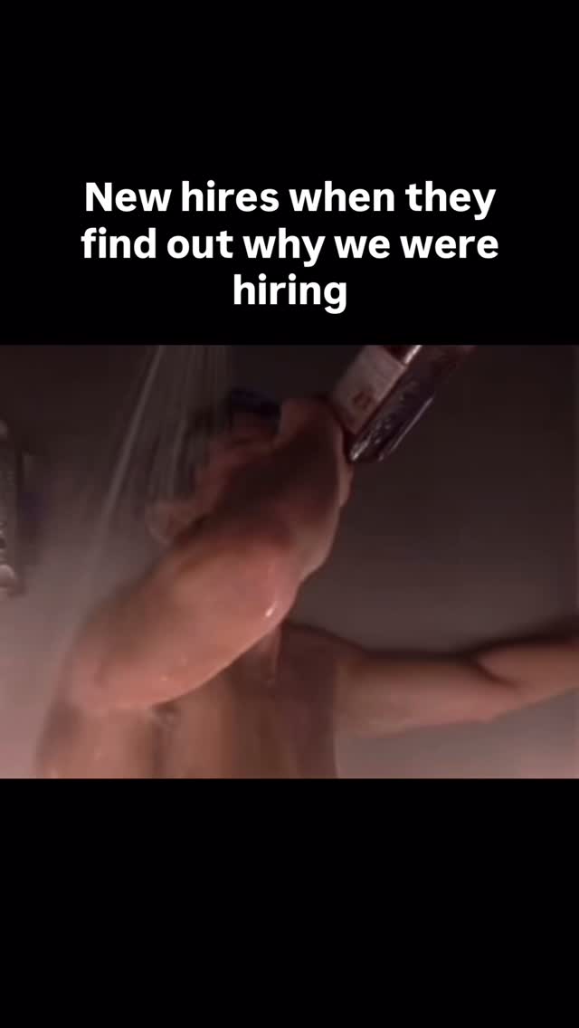 A man in a shower holding a bottle, with text overlayed at the top. The text is white and reads "New hires when they find out why we were hiring". The man's face is partially visible, he appears to be in a shower setting, and the lighting is dim with water droplets visible.