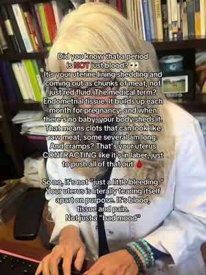 A mid-shot of a woman with blonde hair stands in front of a packed bookshelf.  Text overlays are visible on the screen. The woman is wearing a white lab coat, a black top, and multiple bracelets. The background shows a desk and additional bookshelves containing various books.