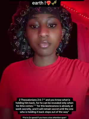 The cover image features a close-up of a woman with dark skin, looking directly at the camera. She has a neutral expression. She wears a patterned head covering. She has a nose ring and a red t-shirt. Text at the bottom of image, and some up top. The background is a dark red color.