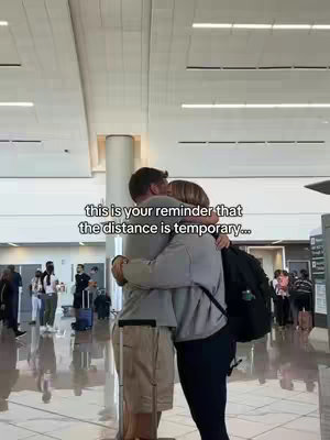 The image captures a tender moment at an airport. A couple is embracing tightly, the woman is in the foreground. The background shows a busy airport terminal, implying a departure or reunion. The lighting is bright, with the couple silhouetted against the open spaces, creating a focus on the emotional connection.