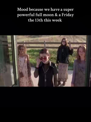 A vertical video image from the movie "The Craft" features four young women standing in front of a green and white painted bus stop. The center woman wears dark clothing and red sunglasses while holding them up to her face. The other three are wearing dresses and long skirts. Text at the top of the image says "Mood because we have a super powerful full moon & a Friday the 13th this week".