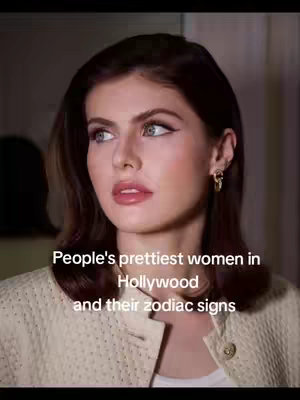 A close-up shot of a woman with fair skin, dark hair, and striking eyes. She is looking slightly off-camera, with a subtle smile. Text overlays indicate the video is about zodiac signs.