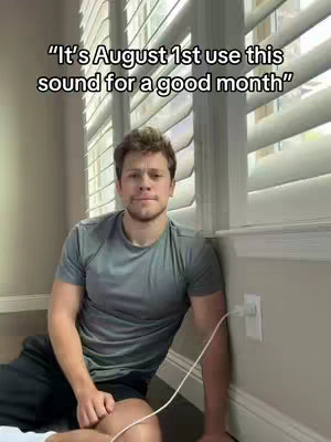 The cover image shows a young man sitting on the floor next to a wall with blinds. He's leaning against the wall, looking at the camera. There is a text overlay over the image that says "'It's August 1st use this sound for a good month'". The color composition is muted, featuring a gray shirt and black shorts on the man, with neutral wall colors