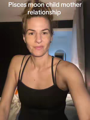 A woman with light skin and blonde hair pulled into a bun is centered in the frame, wearing a black tank top. The background is indistinct but appears to be a domestic setting, with glimpses of a curtain and possibly a bed. Text overlays the image at the top.