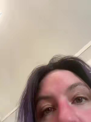 A close-up shot of a person's face from the eyes down, they appear to be in a room with a white ceiling above, with the person's dark hair making a frame in the top. The person has purple highlights and appears to be looking up