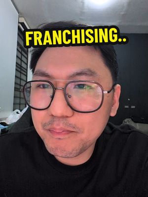 A selfie of a man wearing large-framed glasses, looking straight at the camera with a neutral expression. The background is a blurred domestic setting. Overlay text at the top reads 'FRANCHISING..', framed in a yellow highlighted box.