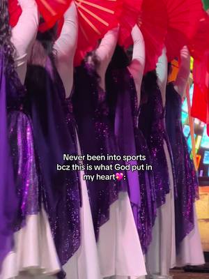 A group of dancers in purple and white dresses, holding red fans, with text overlaid.