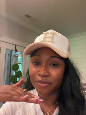 A woman with long dark hair and a white cap with the letter "H" in golden lettering. She's holding up her ring finger with a ring on it, suggesting an engagement or marriage announcement.