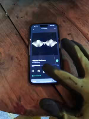 The cover image shows a smartphone displaying a music app, held over a wooden surface. The phone's screen shows the album art with the song title on the foreground. A hand wearing a glove is next to the phone.