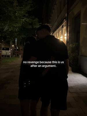 The image shows a nighttime street scene with two people embracing. They are positioned in the center, with their backs to the camera, and are silhouetted against the environment. The background shows a street lit by ambient lighting with buildings. Text overlayed near the bottom reads 'no revenge because this is us after an argument.'