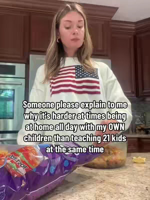 A woman stands in her kitchen, facing the camera with a slightly concerned expression. She is wearing a white sweatshirt with an American flag design. In the foreground, there's a bag of chips on a counter, and a container with food is visible. The background includes kitchen cabinets, appliances (like an oven), and a window.