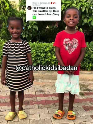 Two young black girls are standing side-by-side, smiling at the camera. The girl on the left is wearing a black and white striped dress, while the girl on the right is wearing a red t-shirt with a heart design. They are standing outdoors in front of a green background.