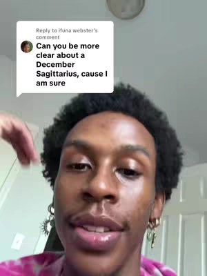 A selfie-style video cover image featuring a young Black man with short, curly hair and a pink tie-dye shirt. He's looking towards the camera and talking. There's a comment overlay on top left corner that reads 'Can you be more clear about a December Sagittarius, cause I am sure'.