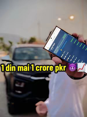 A selfie-style shot featuring a person holding a smartphone in front of a car. The phone displays a leaderboard interface. The background is slightly blurred, suggesting an outdoor setting with hints of buildings and foliage. Overlay text in a yellow box at the bottom of the image that appears to be in an Urdu language. Overall, the composition is centered on the person and the car, giving an emphasis on the content.