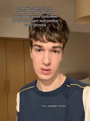A young man with short brown hair is centered in the frame, set against a blurred background of a room. He wears a dark blue t-shirt with yellow accents on shoulders. His expression is neutral, looking directly at the camera. Overlaid text is visible at the top. The text is mirrored at the bottom of the image with text "тгк: хорарстепан".